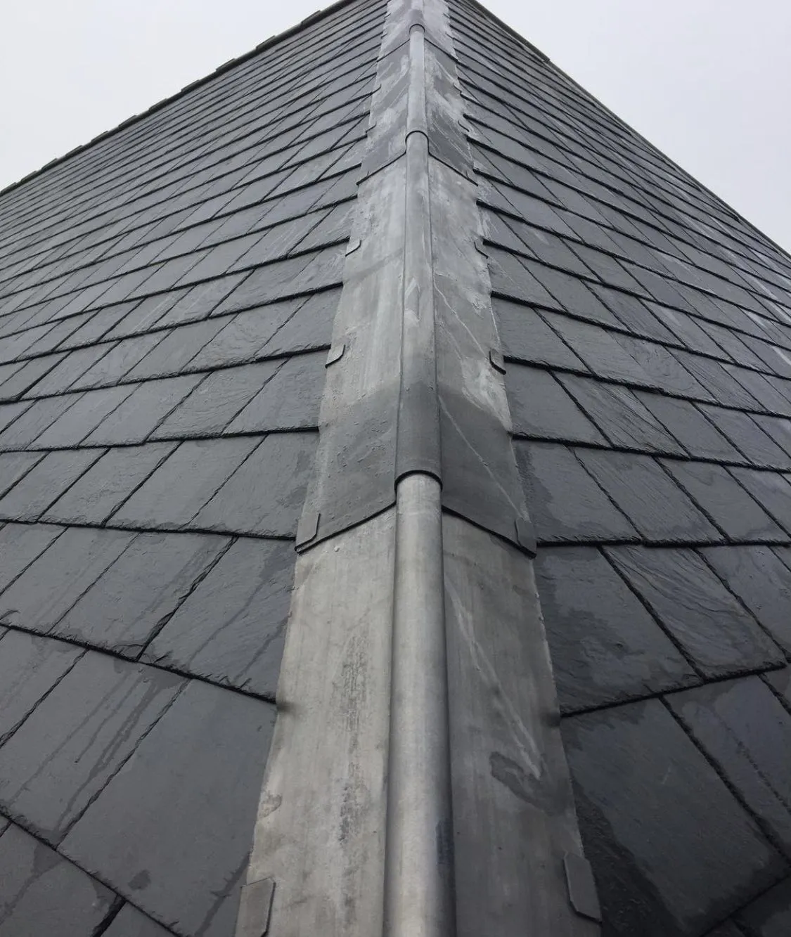 Wet slate at a metal valley, looking up the ridge. No people, no lettering.