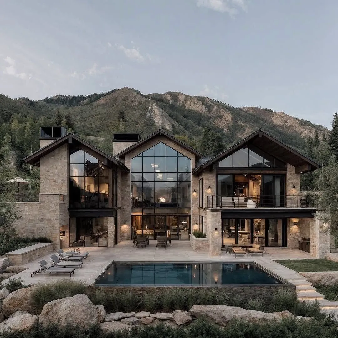 A large mountain house at dusk, dark roof, warm windows, snow on the ground.